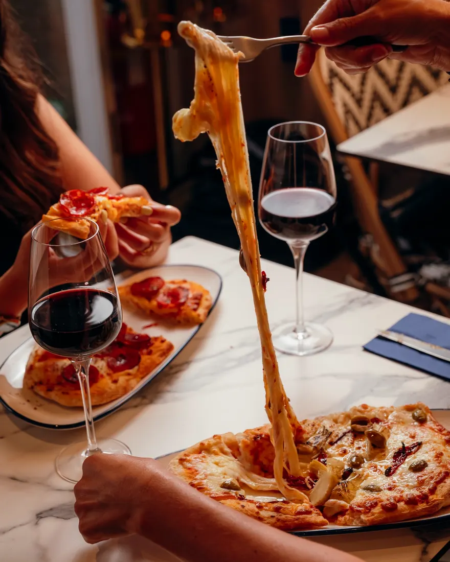 Duas pessoas à mesa num restaurante cliente da Wild, com pizzas e vinho